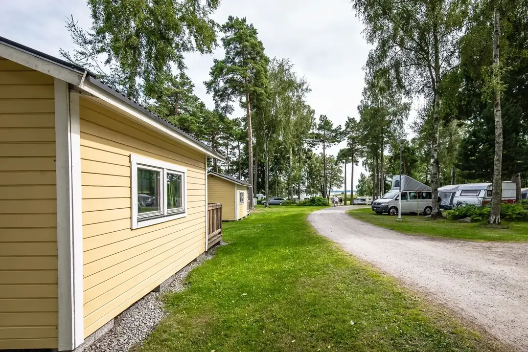 Gul servicebyggnad vid grusväg med husbilar bland träd