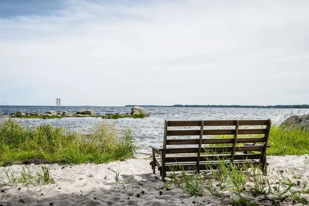 Träbänk på sandstrand med utsikt över havet